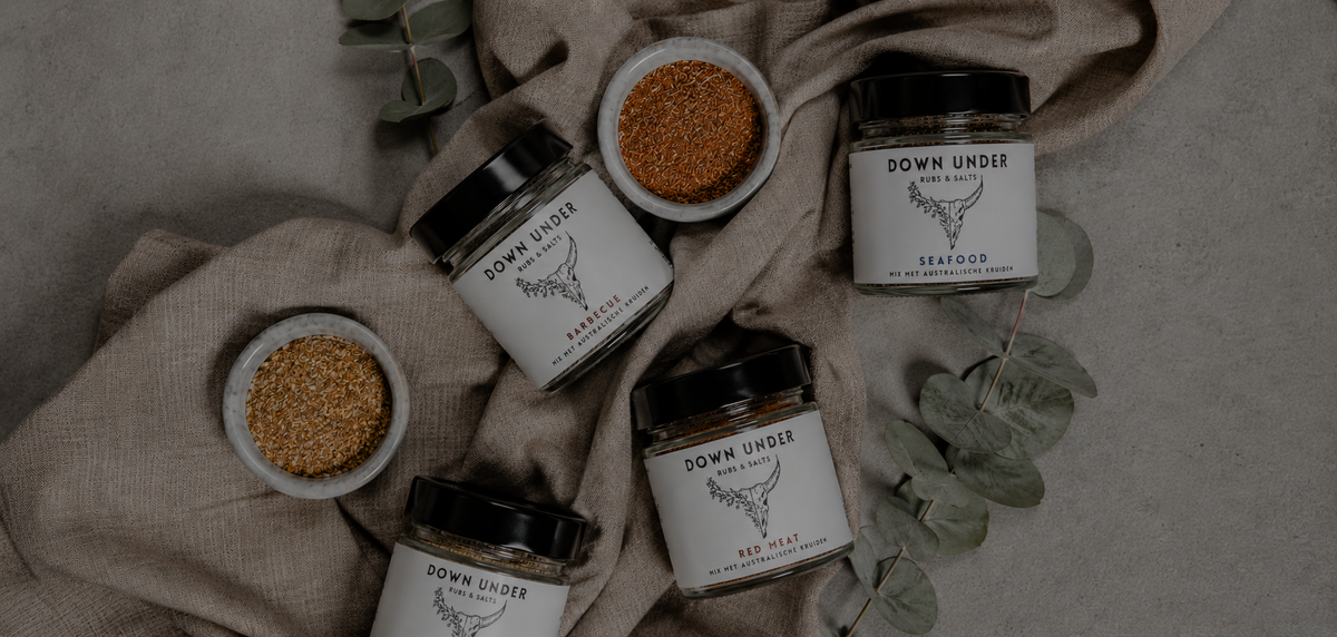 Verschillende glazen potjes met authentieke Australische BBQ-rubs, kruidenmixen en zouten van Down Under Rubs sfeervol gepresenteerd op een jute ondergrond met takjes eucalyptus.